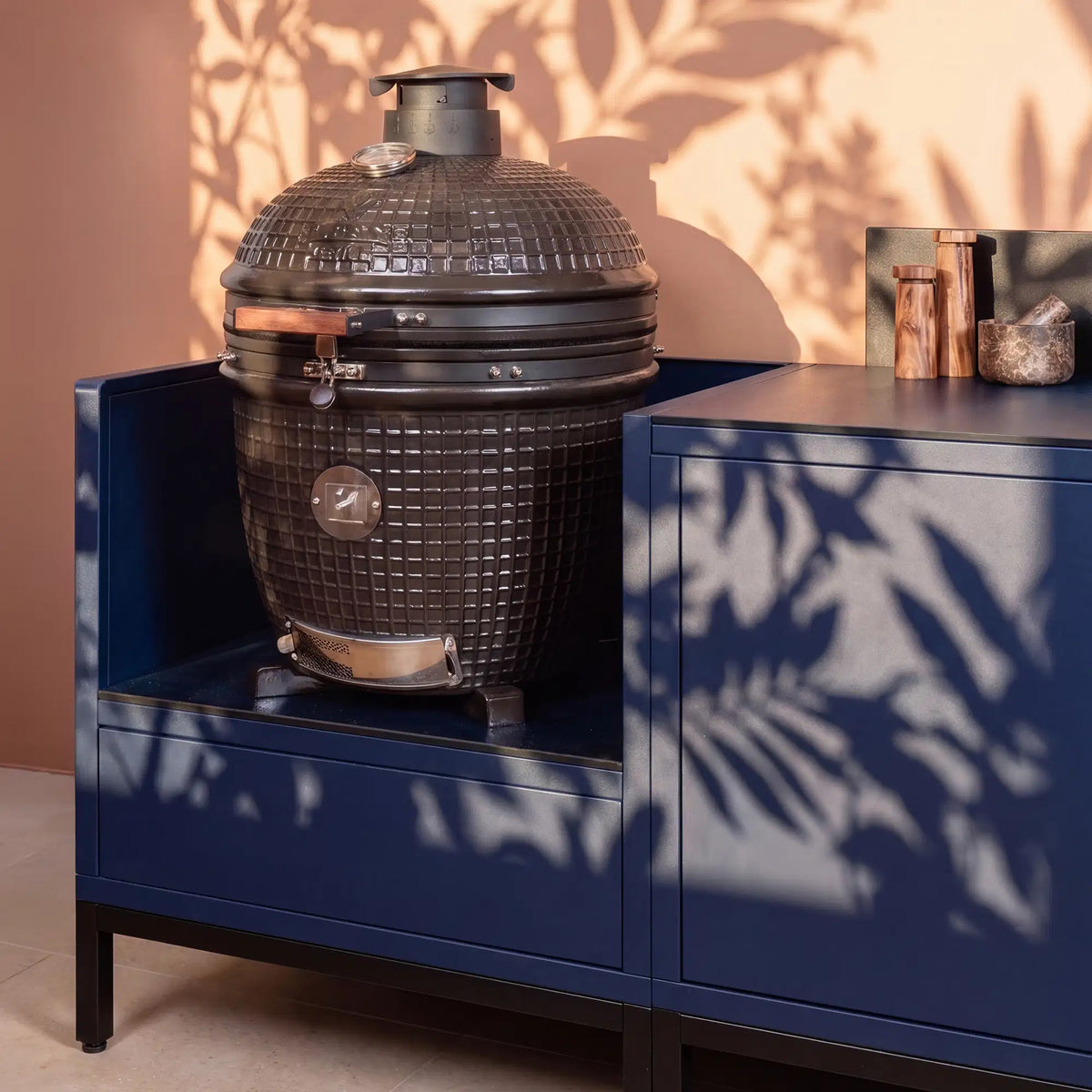 Cucina da esterno Pilotis blu navy con modulo kamado e piano di lavoro in ceramica nera.
::visuel:noir