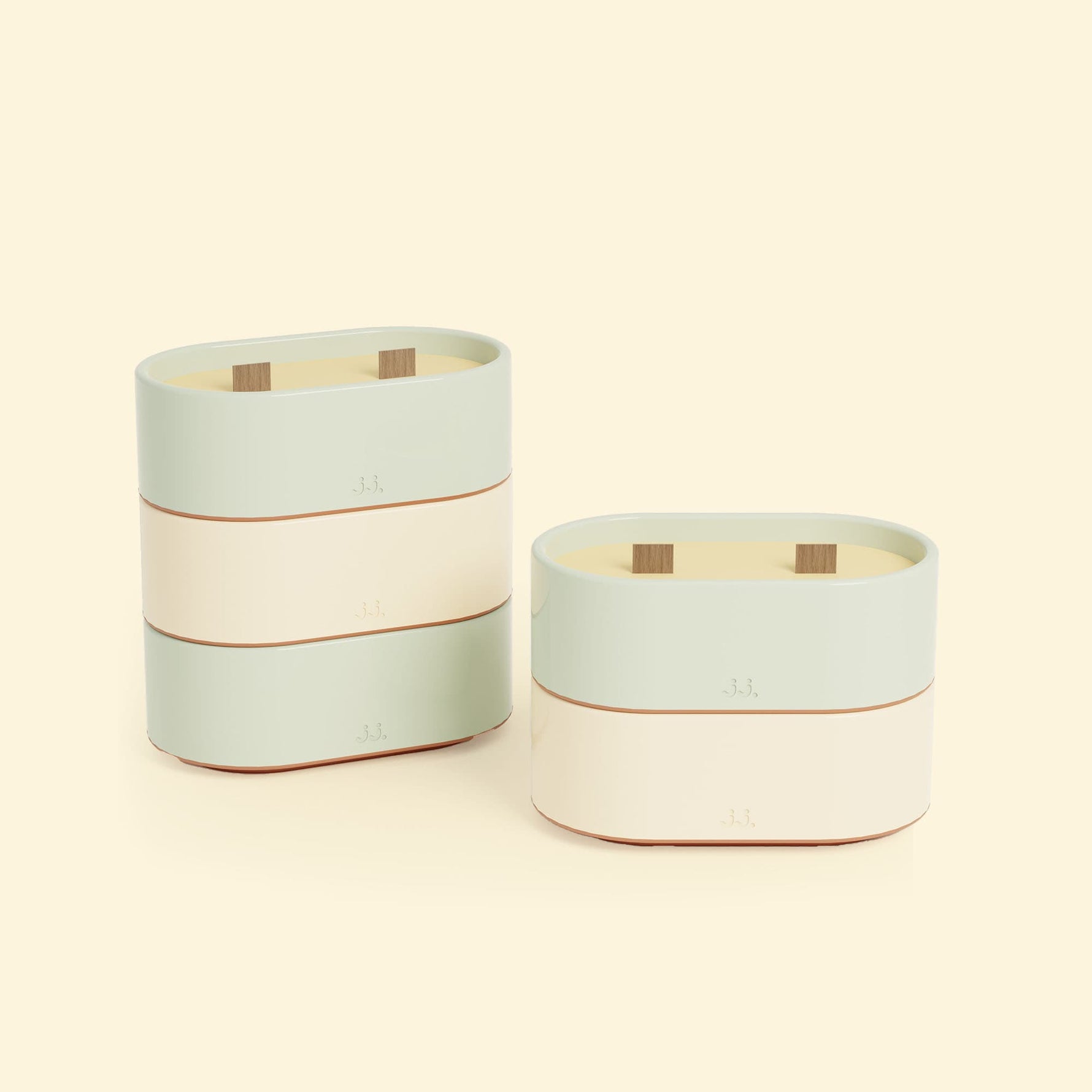 Bougies Totem S Vert d’eau – Citronnelle & Eucalyptus et Beige ivoire – Citronnelle & Citron, deux bougies ovales à double mèche en bois, posées sur un fond beige clair. 