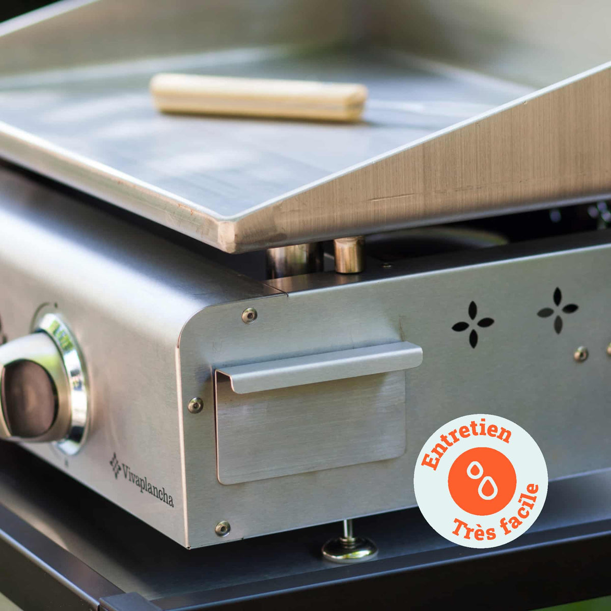 Primo piano sulla plancha Vivaplancha che mostra il raccoglitore di grassi in acciaio inox e uno strumento di pulizia appoggiato sulla piastra, con un badge “Manutenzione molto facile”.