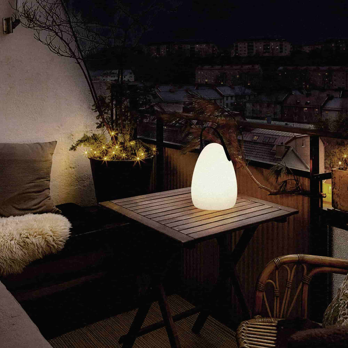 Lampe solaire d’extérieur en forme d’œuf, allumée sur une table en bois sur une terrasse de nuit, diffusant une lumière chaude dans une ambiance cosy.