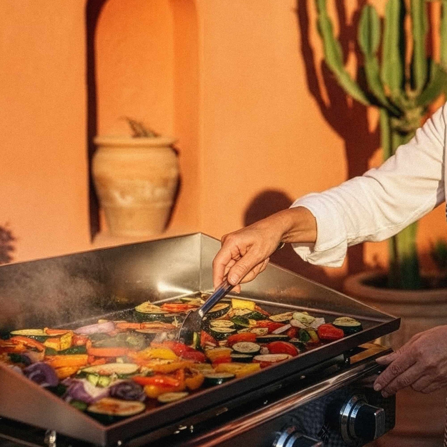 Cuoco che cucina verdure e carni su una plancha in acciaio inox Vivaplancha, controllo perfetto della cottura ad alta temperatura
